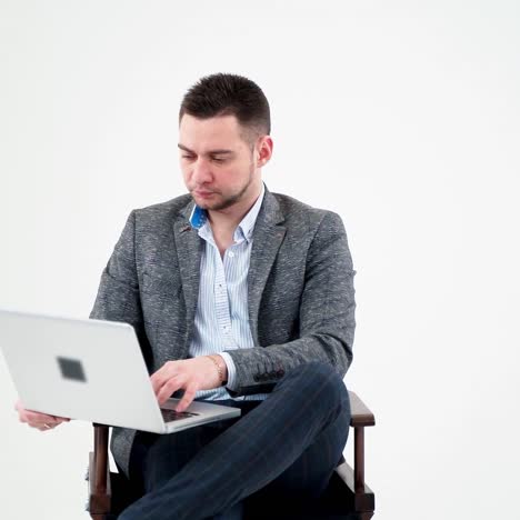 young man sitting in a chair with laptop. handsome businessman in stylish costume working on a modern computer, isolated in studio. freelance work.