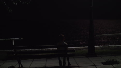 lonely kid sitting on the bench outdoor at night