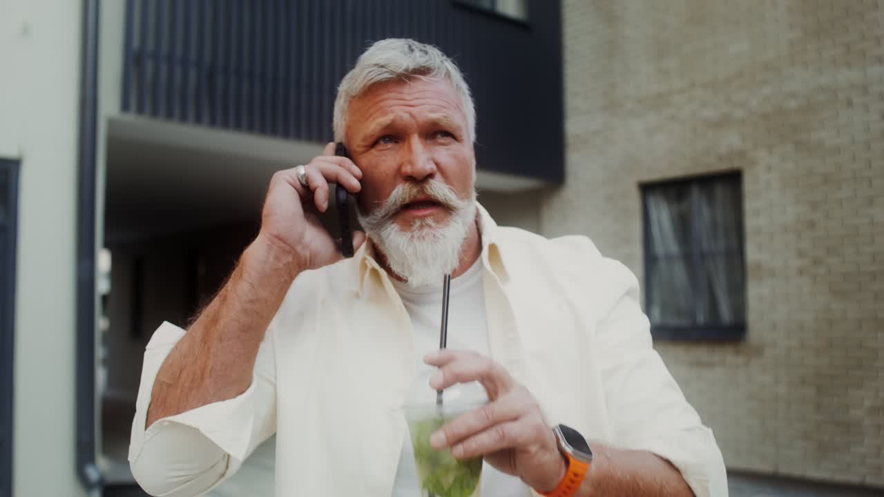 un anciano hablando por teléfono y bebiendo afuera.