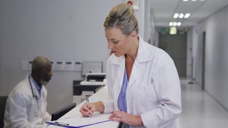 portrait of caucasian female doctor standing at hospital reception smiling at camera