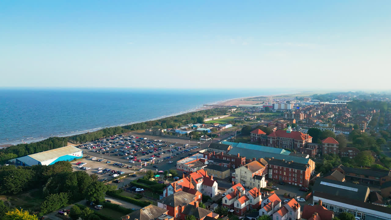 Explore Skegness, Lincolnshire's coastal treasure, through aerial footage, featuring its expansive beach, vibrant tourist area, amusement park attractions, and famous pier during a summer evening