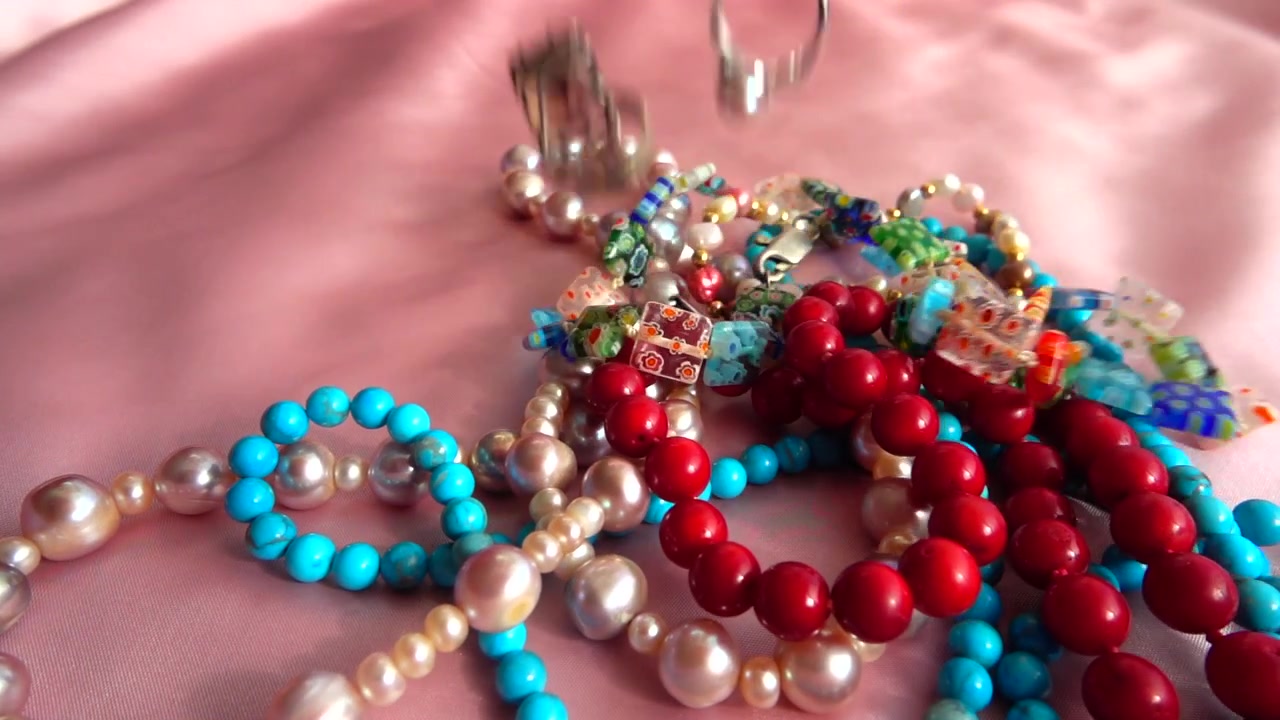 A pearl necklace and rings fall on silk. Slow motion.