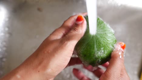 mujer lavando un aguacate en un fregadero de la cocina