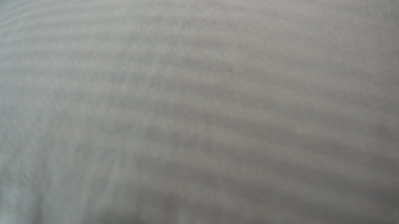 Facialist in navy uniform spreads soft striped cloth over client lying face up on massage bench in bright white treatment room with lamp light, preparing clean comfortable surface for therapy session