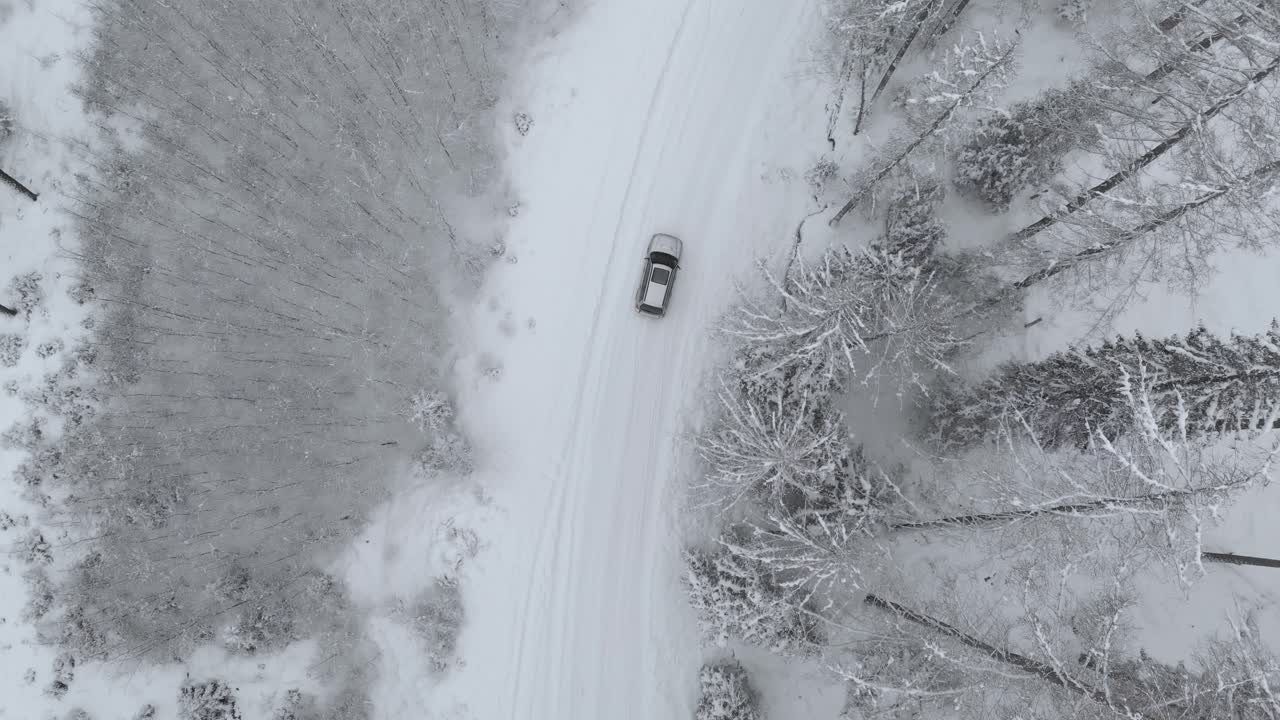 toma de seguimiento aéreo de un camión todoterreno en una carretera nevada girando a la derecha en medio de árboles cubiertos de nieve en un bosque congelado, en un día de invierno - toma de drones, seguimiento, de arriba hacia abajo