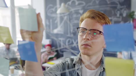 red haired boy in glasses and casual clothes writing notes on the window glass