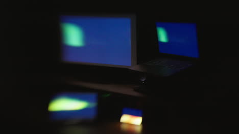 a side angle with selective focus of four digital computer device screens displaying a strobing pattern in a dark room