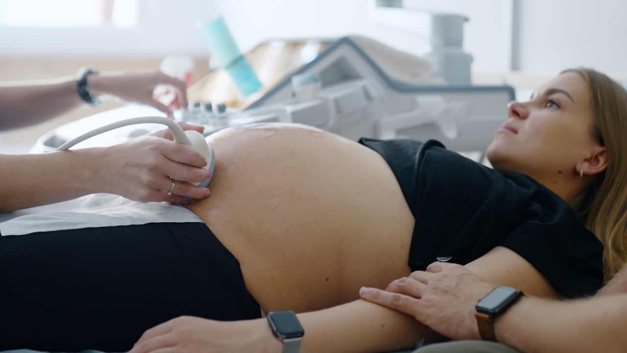Woman is having the ultrasonic scanning of pregnancy. Expecting mom looking attentively on the screen with baby image.