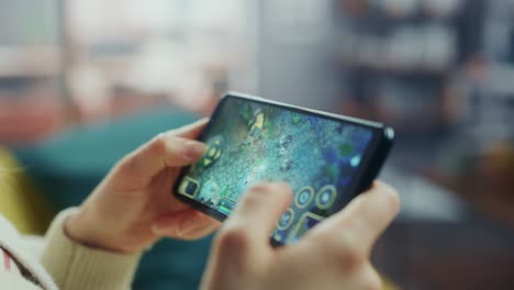 close up on hands playing an rpg strategy video game on a horizontally held smartphone at home living room. feminine hands tapping the mobile phone screen with a colorful game over the internet.