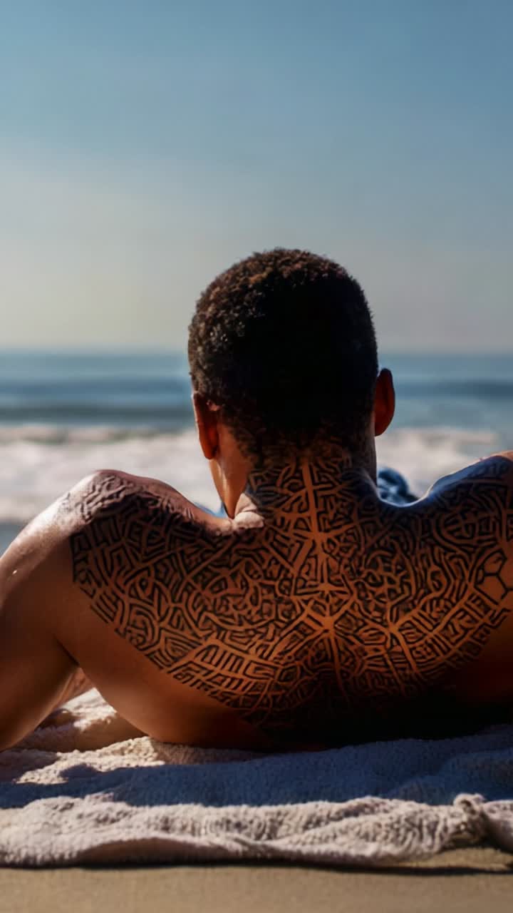 Um homem com tatuagens complexas relaxa na praia, aproveitando o sol e o oceano, capturando um momento sereno de tranquilidade e conexão com a natureza.