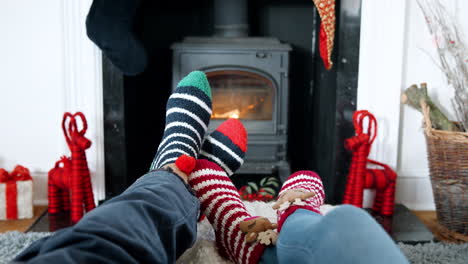 close up de una pareja de mayores con calcetines de navidad calentando los pies en la estufa de leña