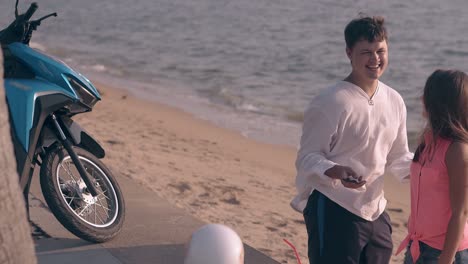 couple with brown hair stands on beach and looks at photo