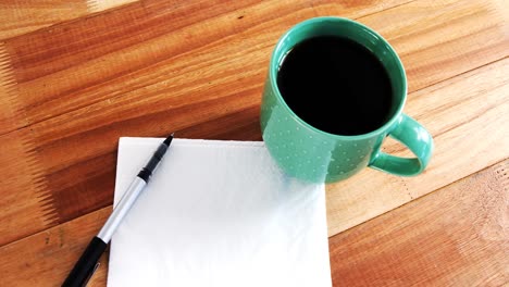 Close-up-of-coffee-mug-with-blank-paper-and-pen