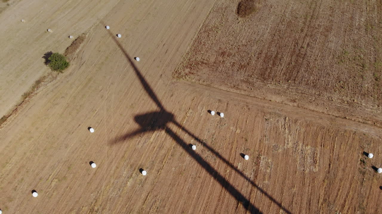 Aerial View of Wind Turbine Shadow Over Hay Bales Field