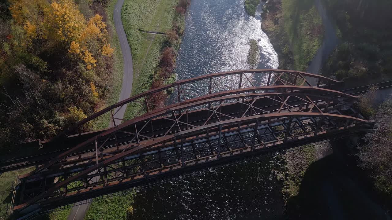 Descending Drone reveals rusty arch metal railway bridge over river