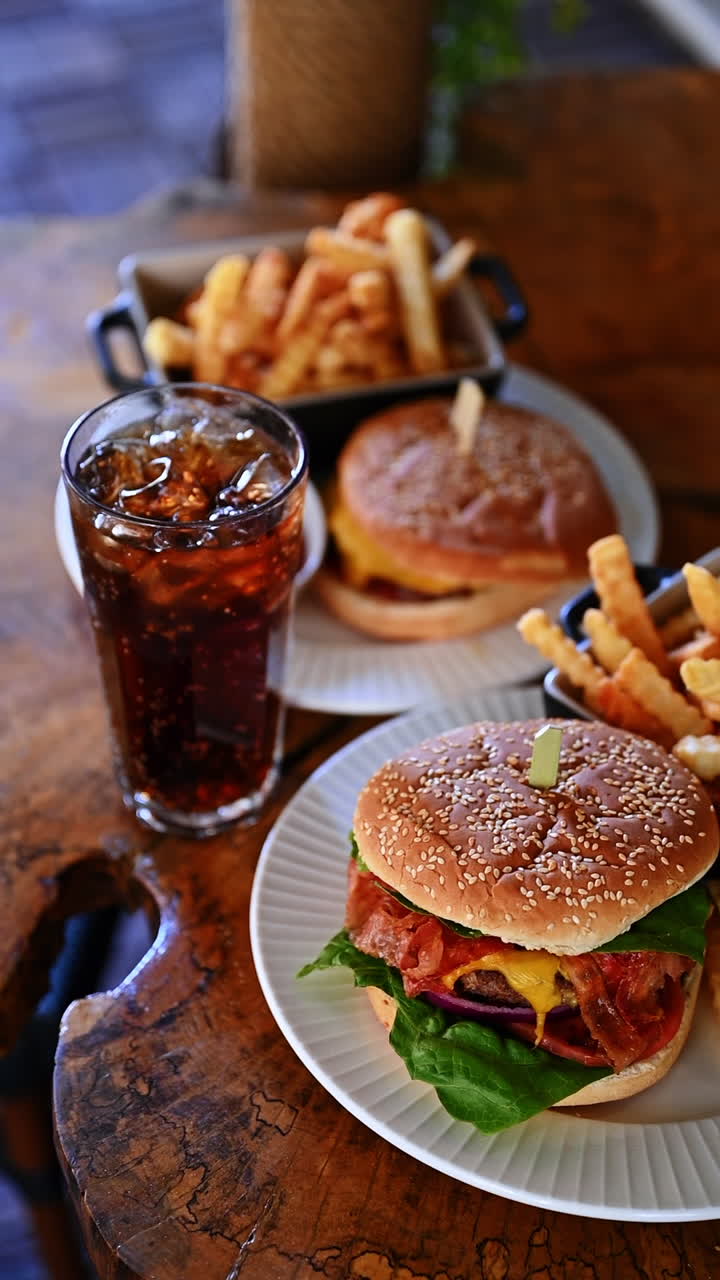 Classic cheeseburger with fries and soda on rustic wooden table. Fresh cheeseburger with fries and cola drink on plate in cafe setting with warm light