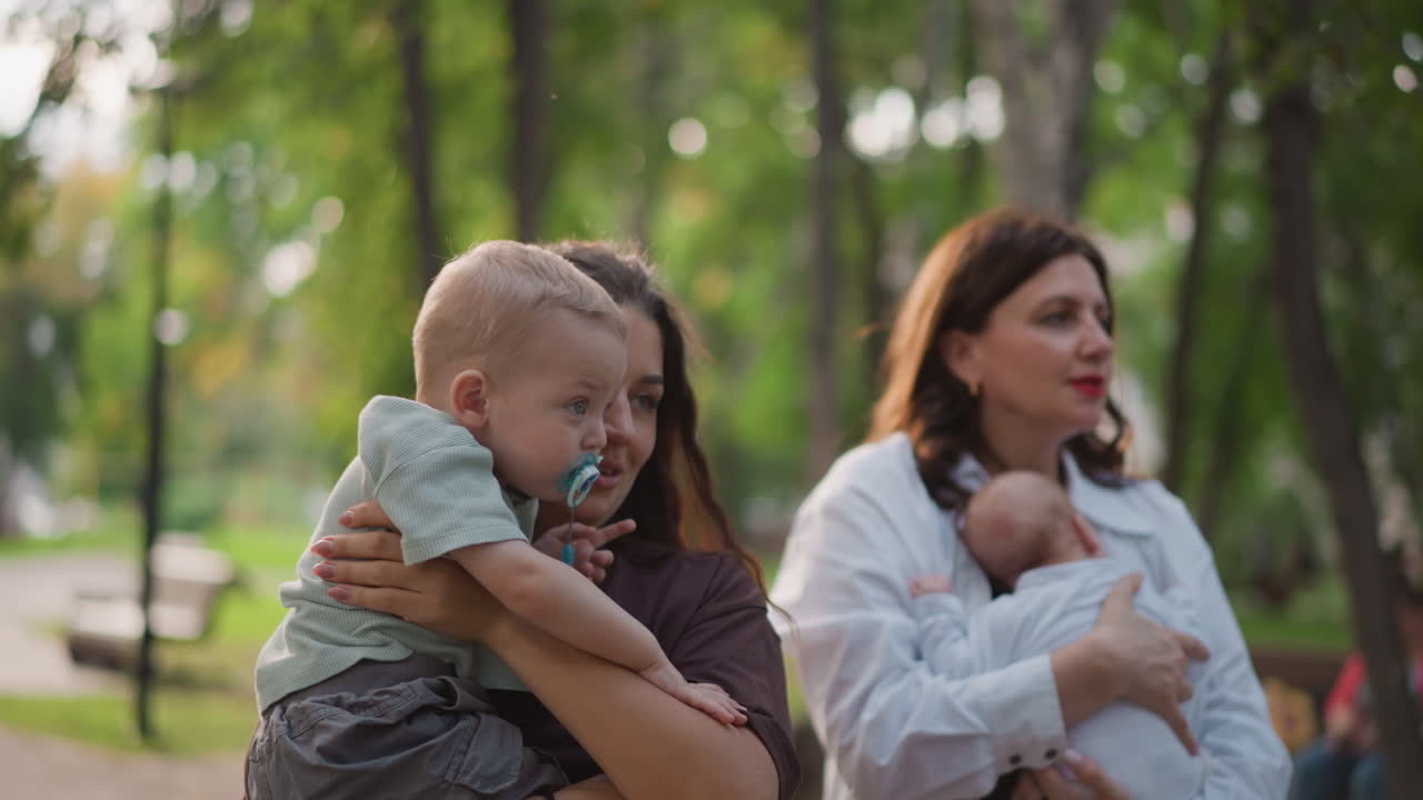 Eltern halten Kinder sanft draußen. Mutter und Vater umarmen Kinder liebevoll unter belaubten Ästen im Freien. Elternfiguren wiegen ihre Kleinen zärtlich in einer friedlichen Außenumgebung