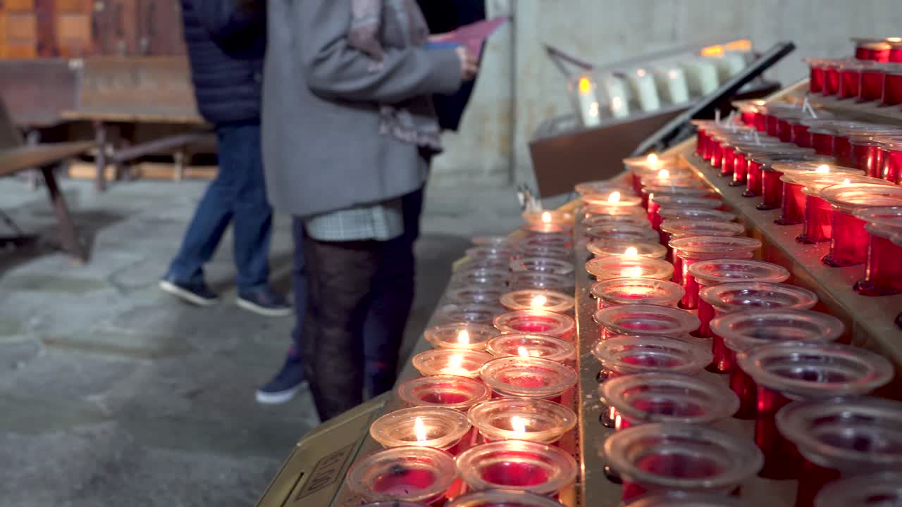 Persone che accendono candele sulle macchine all'interno di una cattedrale, desideri e preghiere ai santi rappresentati