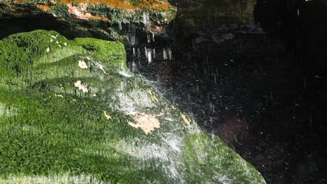 slow motion of a small waterfall smashing onto a mossy green rock