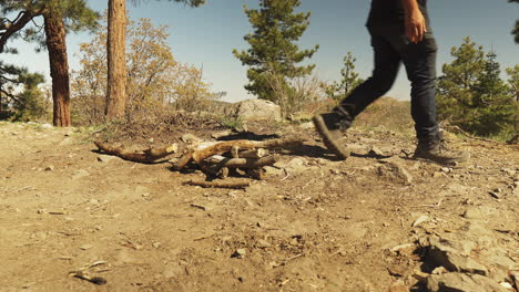 low angle man walks to the frame throws the wood caught on the ground and leaves the frame view of legs