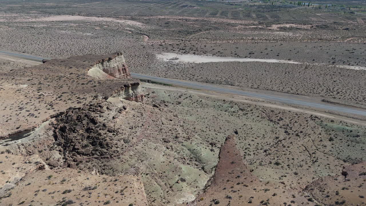 High-altitude drone shot of road winding through Argentina's desert landscape, with sandy plains, cliffs, and rugged terrain. Shot on 4K at 60fps.