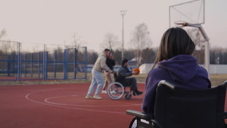 disabled woman in wheelchair recording with smartphone to her friends playing to basketball