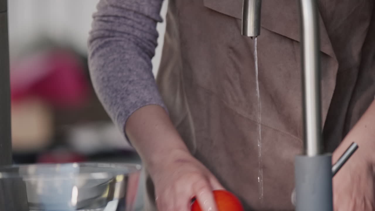 한 여자가 수도꼭지에서 나오는 물줄기 아래 토마토를 씻는다