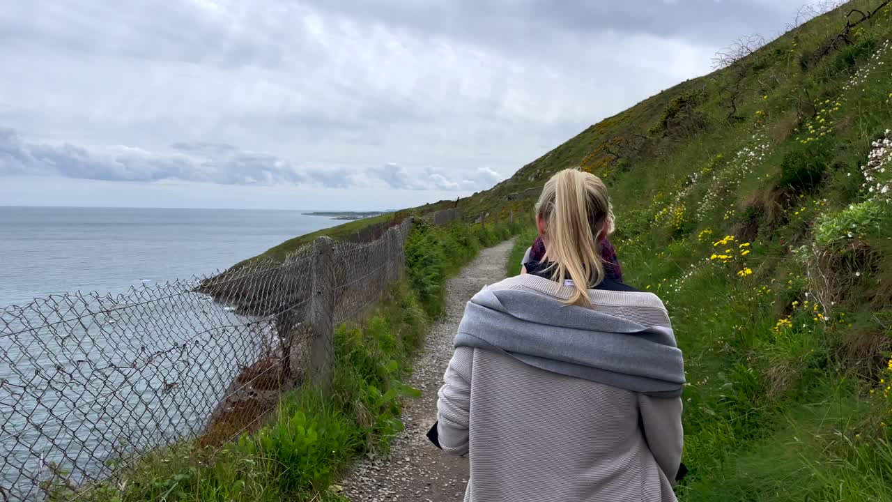 흐린 날 동안 아일랜드 절벽과 해안선 위에 있는 등산객 그룹을 보여주는 슬로우 모션 샷