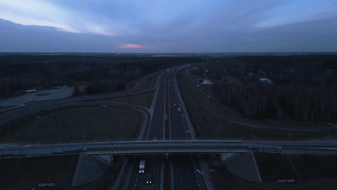 An urban expressway with bridges and on- and off-ramps and little traffic. Camera tilt up movement reveals horizon with early evening sky