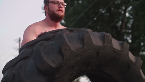 man pushing large tire during exercise, medium shot, slow motion