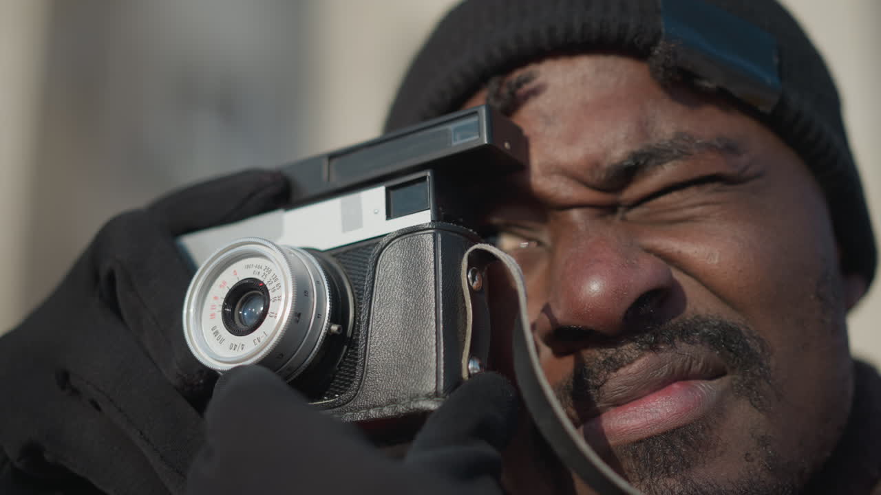 close up of photo enthusiast eyes fixed on camera adjusting lens capturing scene under bright sunny sky with gloves on winter coat in snowy urban setting with crisp contrast composition on cold day