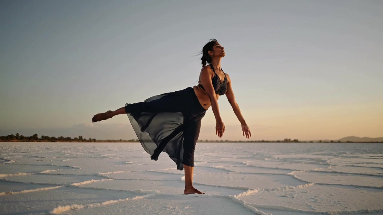 Shifting weight dancer lifting right leg on salt flats at sunset, practicing balance in sheer skirt
