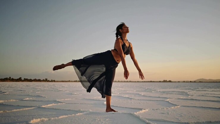 Shifting weight dancer lifting right leg on salt flats at sunset, practicing balance in sheer skirt