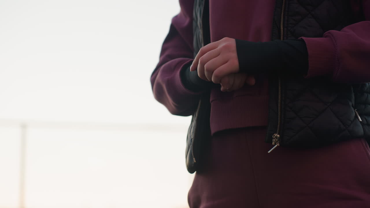 Gym enthusiast squatting with arms extended forward and intense focus on face during outdoor workout on urban sports court at sunset, modern apartment facades and evening sky blurred in background