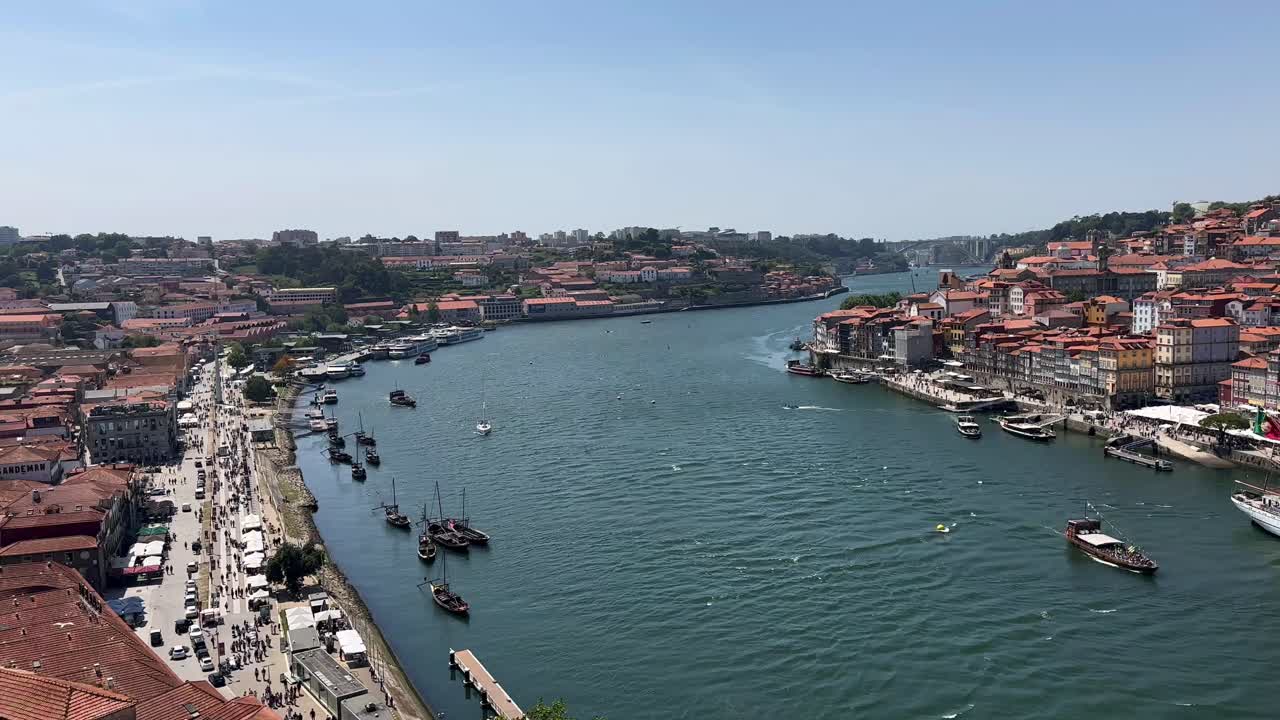 Panoramic shot over city of Oporto with Douro River, old town buildings and rabelo boats during sunny day with blue sky - view from top of Ponte Dom Lu&iacute;s I, Portugal