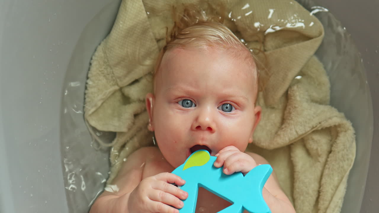 Baby lies in a plastic tub and bathes. Bathing a child in clear water. Child lies in water