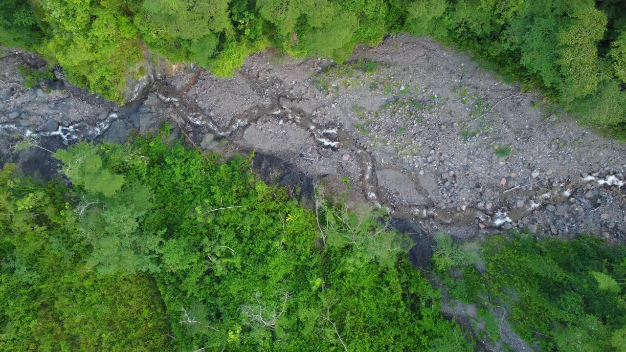 una vista de las aves de arriba hacia abajo siguiendo un lecho de río seco en un bosque tropical con una pequeña corriente de agua que fluye, risaralda, colombia