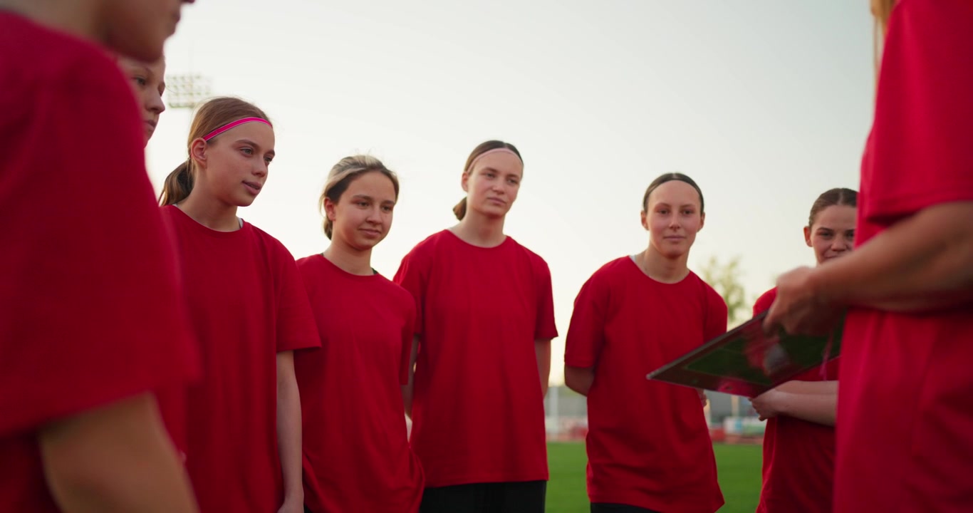 Joven equipo de fútbol femenino escuchando las instrucciones del entrenador en el campo