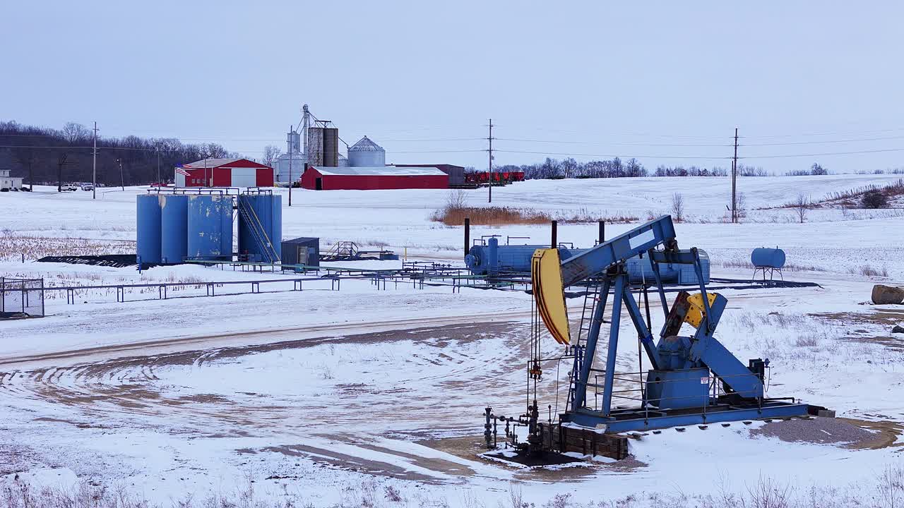 Oil pumpjack extracting crude oil in a Michigan winter field with storage tanks in background, USA