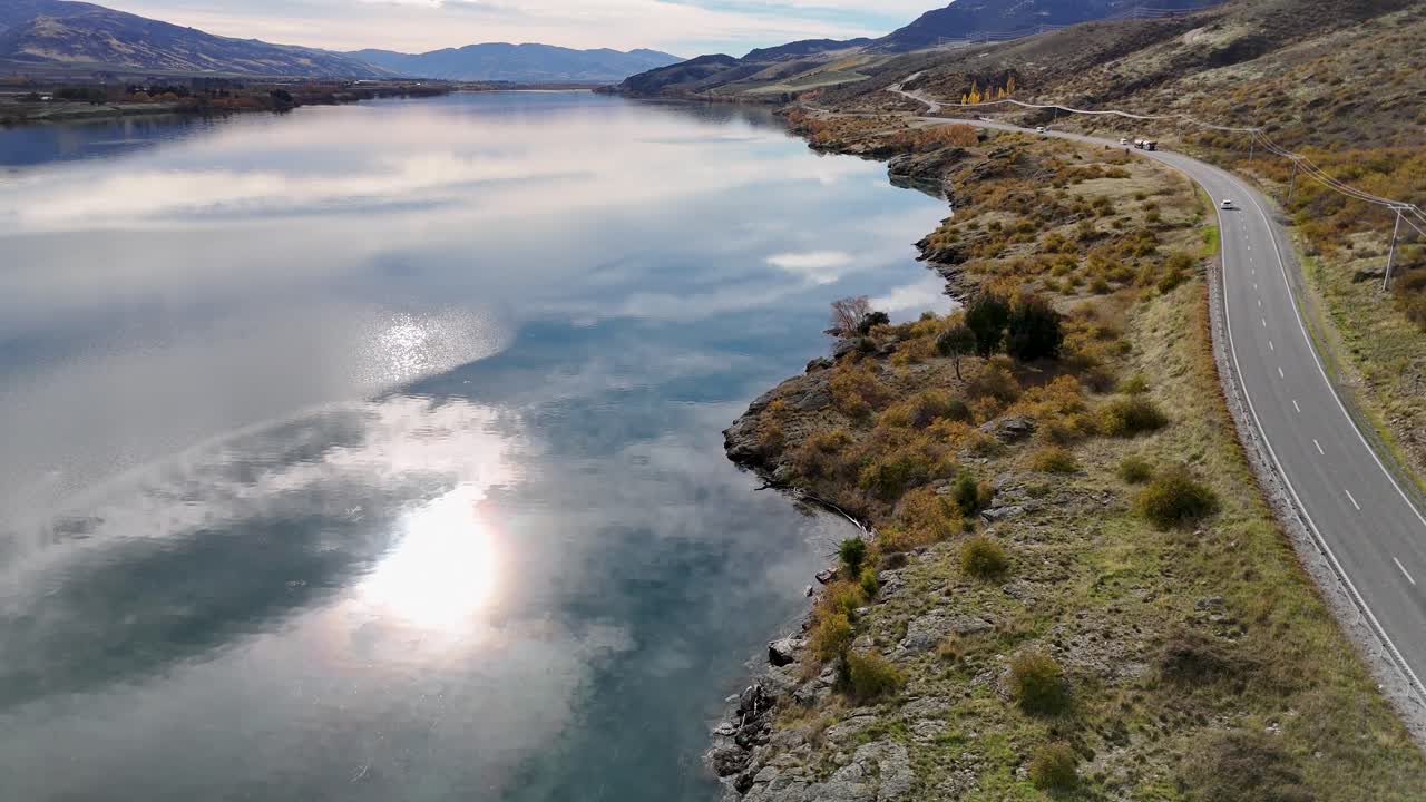 Aerial view of Lake Dunstan with a winding road, captured in autumn with clear reflections and serene landscape