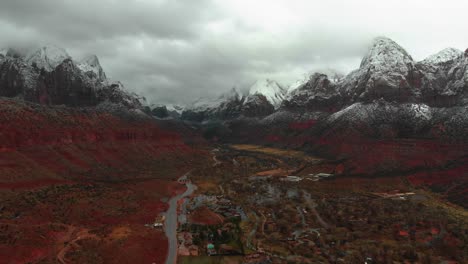 aerial push in shot of stunning snow covered, red rock mountains peaking through the clouds with a road cutting through.