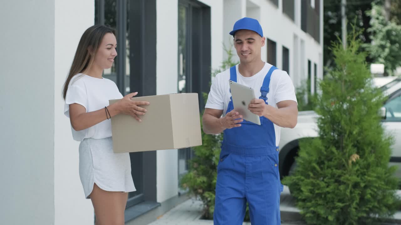 una mujer hermosa conoce a un repartidor que le da una caja de paquetes al lado de su casa, ella firma una firma electrónica en una tableta. concepto de mensajero, entrega a domicilio, compras en línea