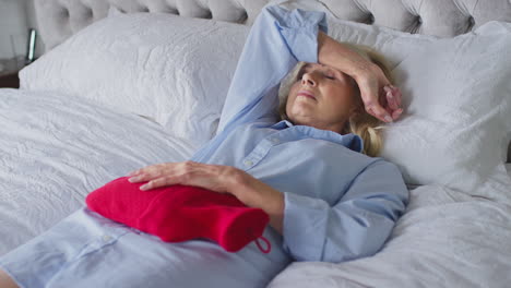 menopausal mature woman lying in bed with hot water bottle at home