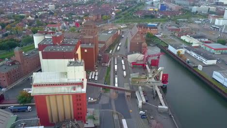 Aerial-flyover-shipyard-of-Bremen-with-old-buildings,-cranes-and-container-during-cloudy-day