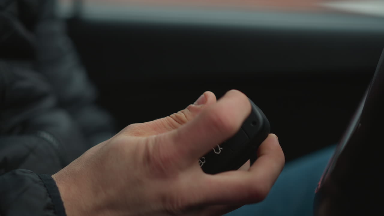 Close up of motorist pressing button on car key fob causing metal key to flip out inside vehicle cabin focusing on hand gesture and dashboard blur as driver prepares for engine start
