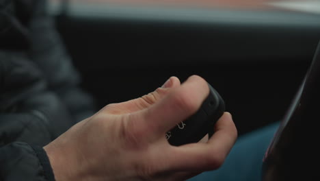 close up of motorist pressing button on car key fob causing metal key to flip out inside vehicle cabin focusing on hand gesture and dashboard blur as driver prepares for engine start