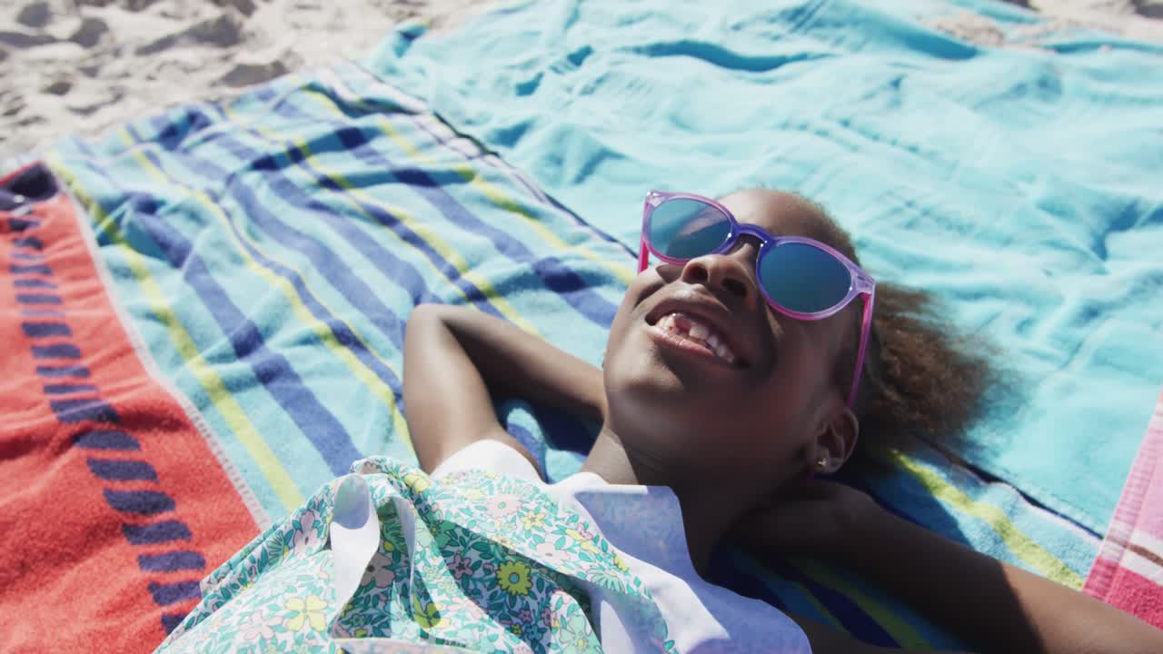 Video af glad afrikansk-amerikansk pige, der slapper af på et tæppe på stranden.