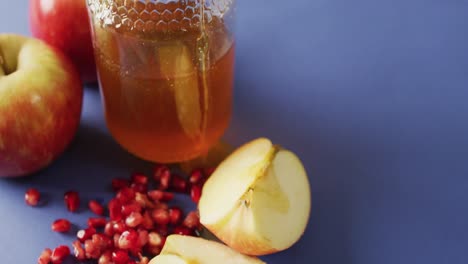 video de miel en frasco, arándanos, manzanas y rodajas de manzana sobre una superficie azul