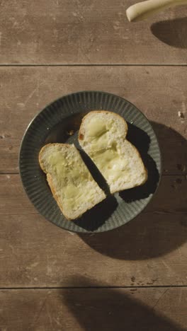 Vertical-Video-Overhead-Shot-Of-Person-Eating-Freshly-Baked-Bread-With-Butter-On-Wooden-Table-With-Hot-Drink