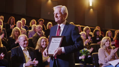 man receiving an award on stage to applause from an audience